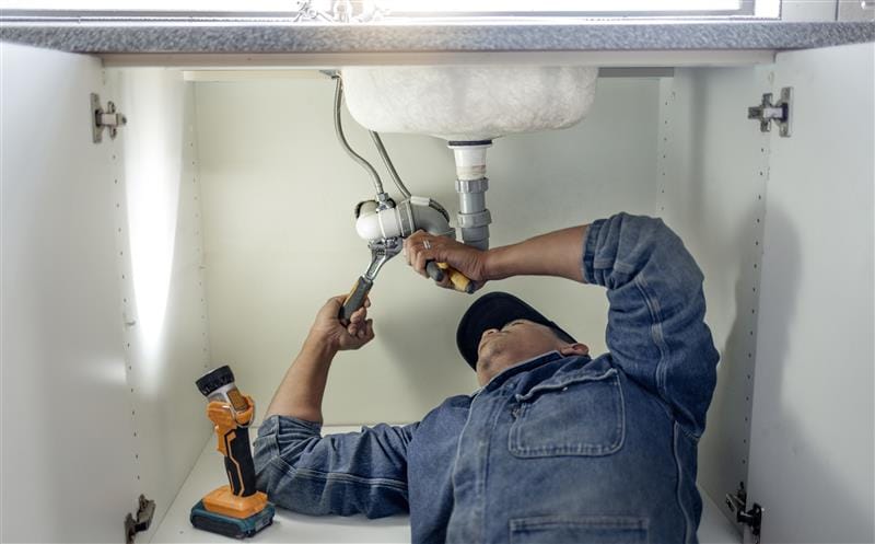 Plumber repairing pipes beneath a bathroom sink in Bloomington
