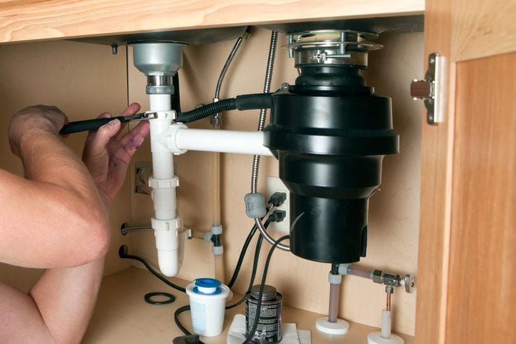 Plumber installing a garbage disposal beneath a kitchen sink in Bloomington