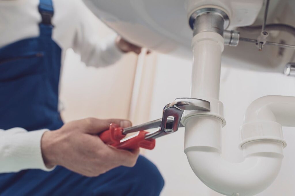 Plumber repairing a white drain pipe beneath a sink in Bloomington