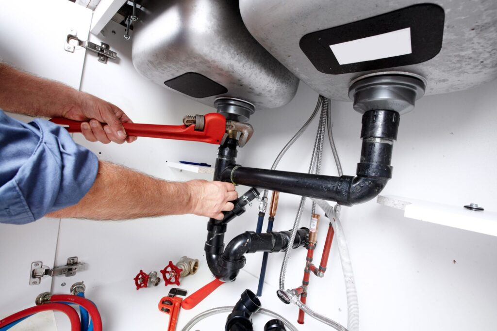 Plumber repairing drain pipes beneath a kitchen sink in Bloomington